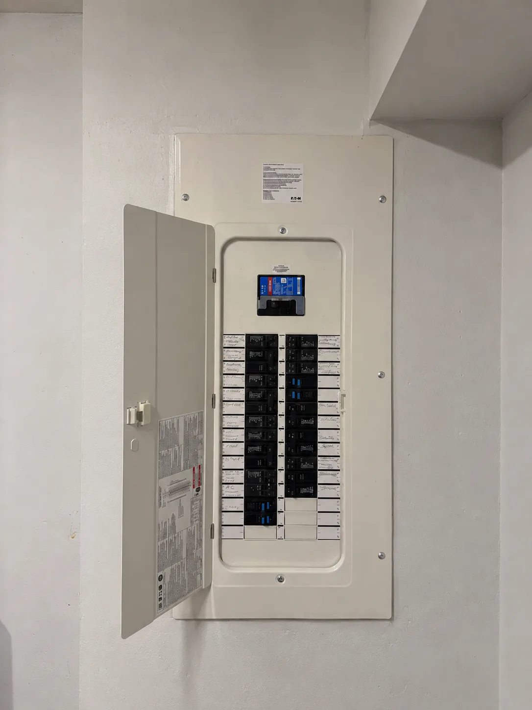 A new Eaton panel Copper Bee installed on a plain white wall, its door swung open on a column of hand-labelled breakers.